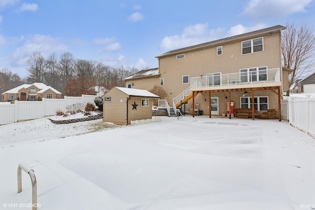 snow covered property featuring a storage unit, a fenced backyard, stairway, and an outbuilding