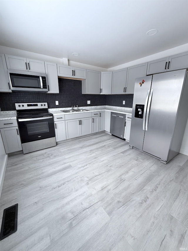 kitchen featuring sink, light hardwood / wood-style flooring, appliances with stainless steel finishes, gray cabinets, and backsplash