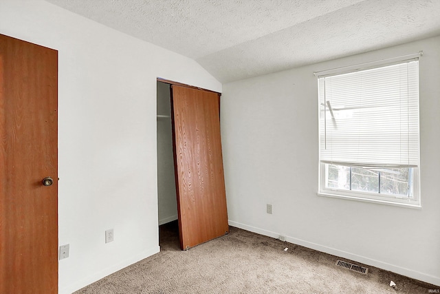 unfurnished bedroom featuring light carpet, a textured ceiling, a closet, and lofted ceiling