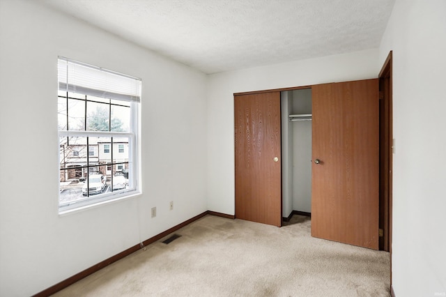 unfurnished bedroom featuring a textured ceiling, light carpet, and a closet