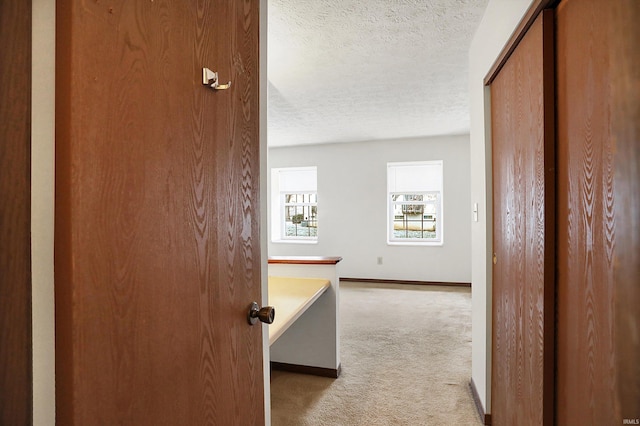 hallway featuring light colored carpet and a textured ceiling