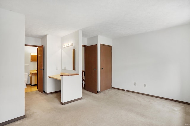 unfurnished bedroom with light carpet, a textured ceiling, and ensuite bath