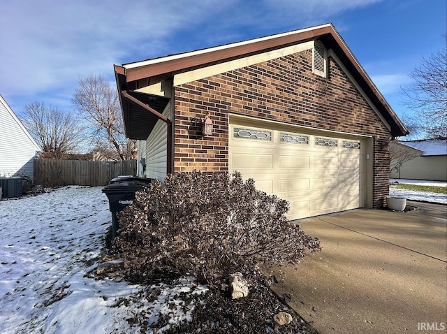 snow covered property with a garage and central AC unit