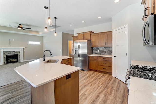 kitchen featuring stainless steel appliances, ceiling fan, sink, pendant lighting, and a center island with sink