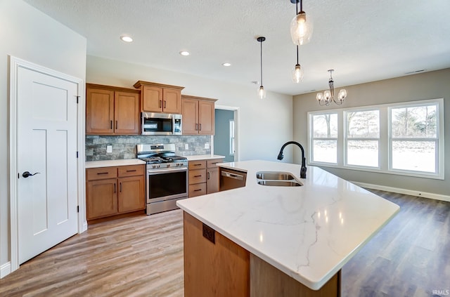 kitchen with pendant lighting, sink, stainless steel appliances, and a kitchen island with sink