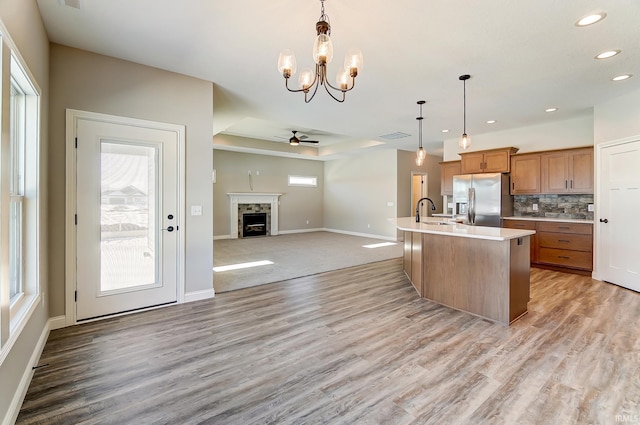 kitchen with decorative backsplash, stainless steel fridge, ceiling fan with notable chandelier, decorative light fixtures, and an island with sink