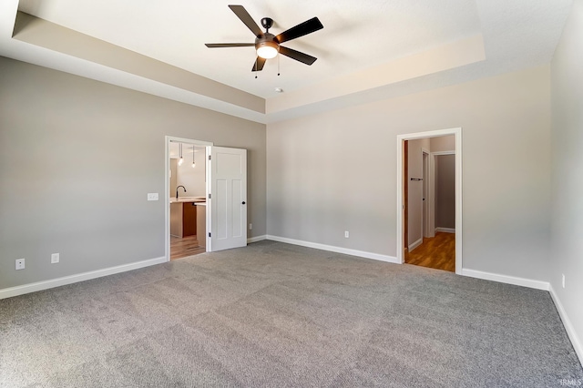 unfurnished bedroom featuring a tray ceiling, ceiling fan, carpet flooring, and ensuite bathroom