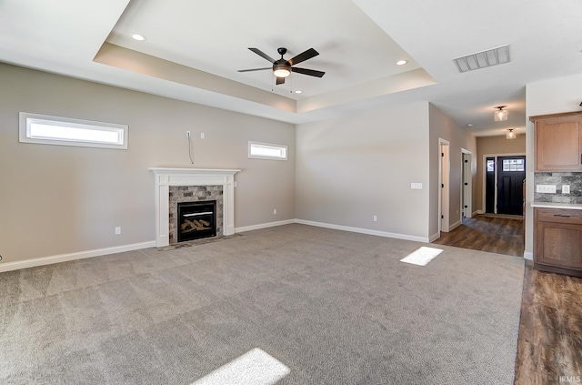 unfurnished living room featuring a fireplace, dark carpet, a raised ceiling, and ceiling fan