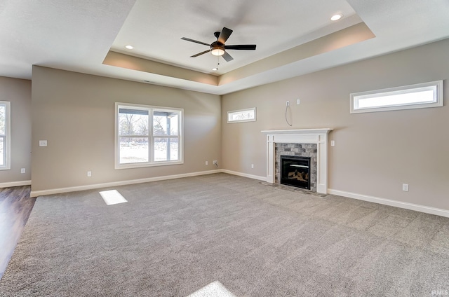 unfurnished living room with a tile fireplace, light carpet, a raised ceiling, and ceiling fan