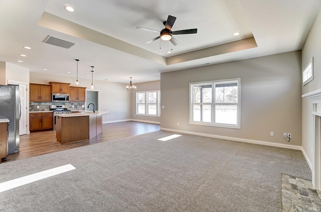 kitchen with appliances with stainless steel finishes, ceiling fan with notable chandelier, sink, pendant lighting, and a center island with sink