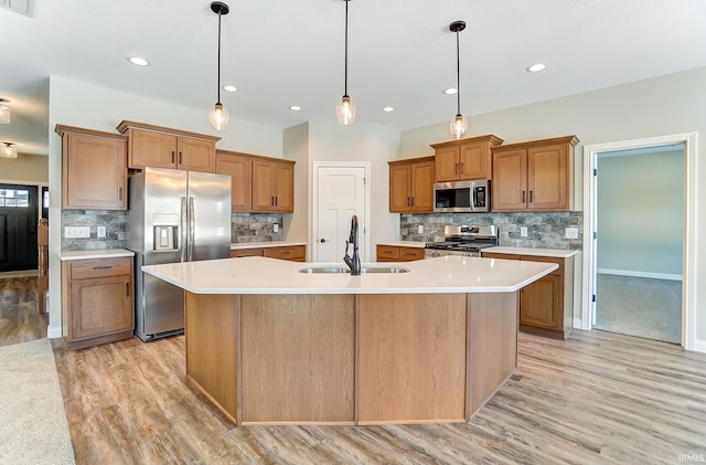 kitchen with sink, hanging light fixtures, an island with sink, appliances with stainless steel finishes, and tasteful backsplash