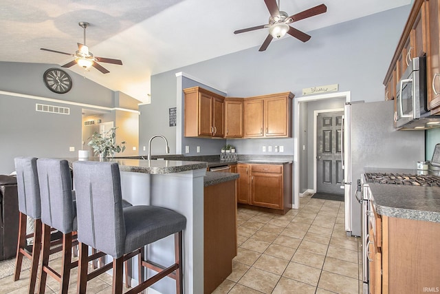 kitchen featuring kitchen peninsula, a kitchen bar, stainless steel appliances, and vaulted ceiling