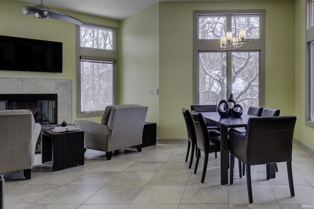 dining space featuring a tile fireplace, plenty of natural light, light tile patterned floors, and ceiling fan with notable chandelier