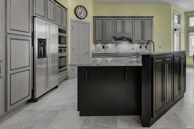 kitchen featuring gray cabinetry, decorative backsplash, high quality fridge, light tile patterned flooring, and light stone counters