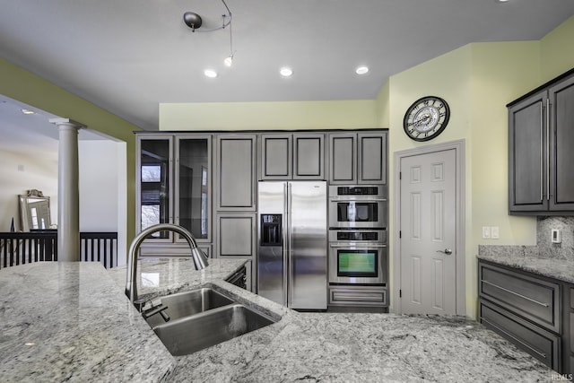 kitchen with light stone countertops, appliances with stainless steel finishes, backsplash, decorative columns, and sink