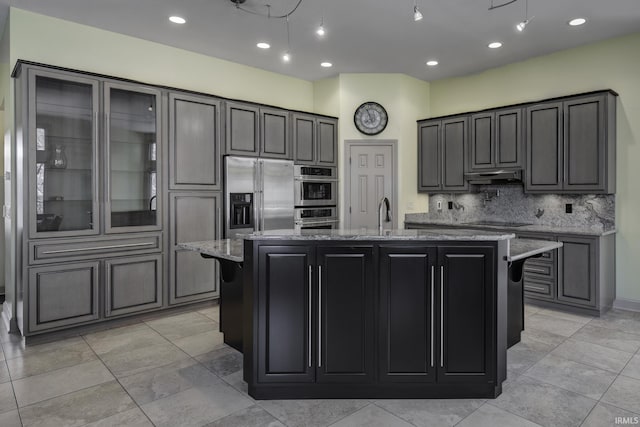 kitchen featuring light stone countertops, appliances with stainless steel finishes, decorative backsplash, a kitchen island with sink, and sink