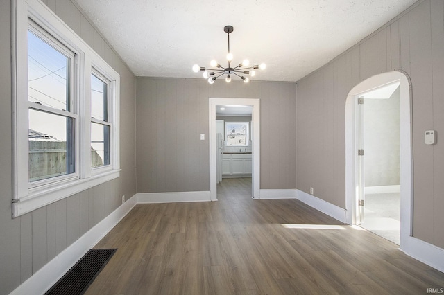 unfurnished dining area with a chandelier, a textured ceiling, and hardwood / wood-style flooring