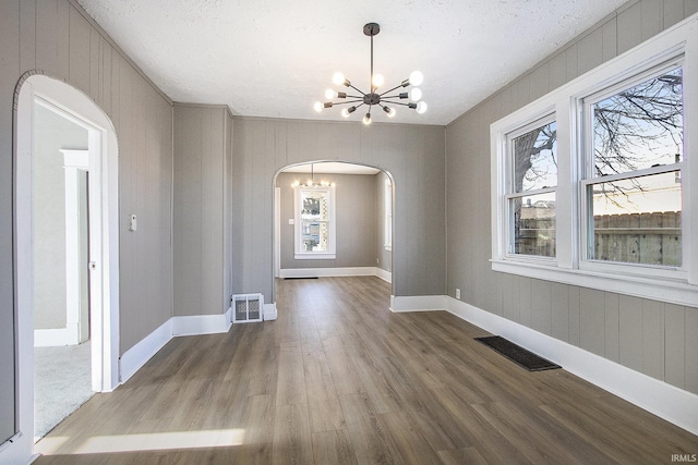 unfurnished dining area with wood-type flooring, a textured ceiling, and an inviting chandelier