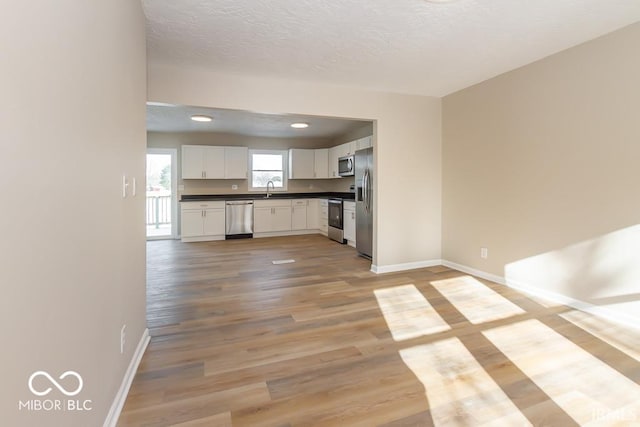 kitchen featuring white cabinets, sink, a textured ceiling, appliances with stainless steel finishes, and light hardwood / wood-style floors