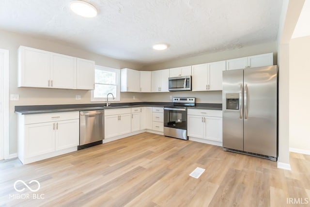 kitchen with sink, light wood-type flooring, a textured ceiling, white cabinetry, and stainless steel appliances