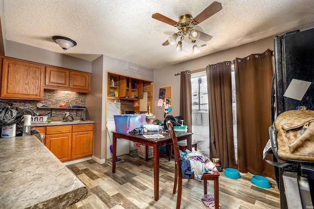 kitchen featuring ceiling fan, sink, tasteful backsplash, a textured ceiling, and light wood-type flooring