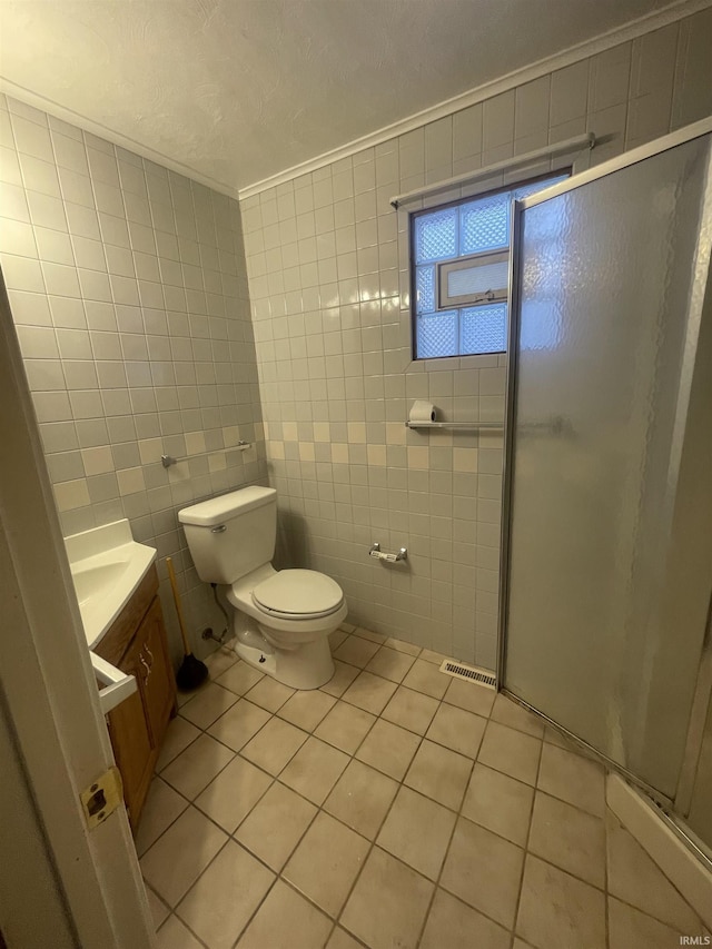 bathroom with tile patterned floors, toilet, a shower with door, vanity, and tile walls