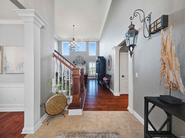 foyer featuring tile patterned floors, crown molding, decorative columns, and a notable chandelier