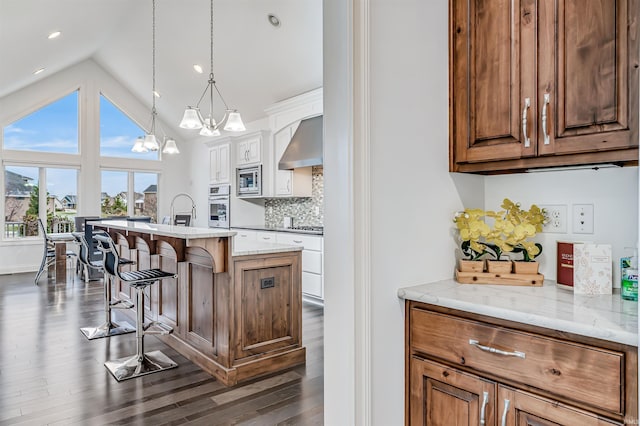 kitchen featuring wall chimney exhaust hood, a kitchen breakfast bar, a notable chandelier, vaulted ceiling, and a kitchen island with sink