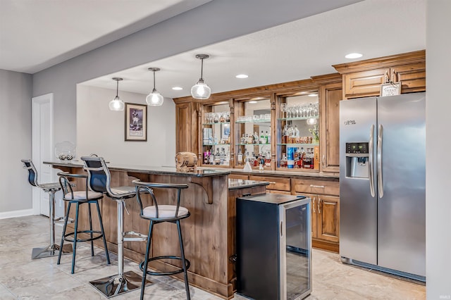 bar with dark stone countertops, stainless steel fridge, hanging light fixtures, and wine cooler