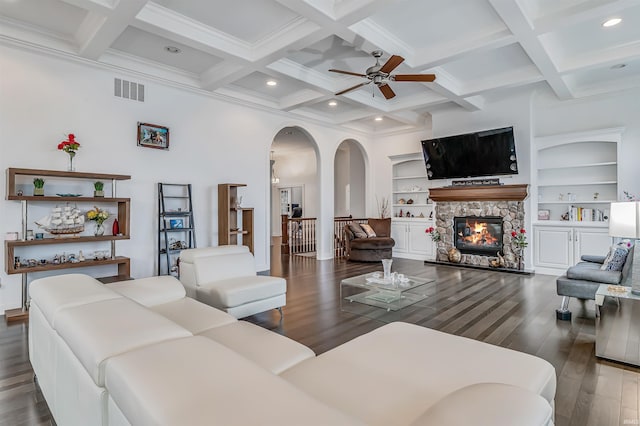 living room with built in shelves, ceiling fan, dark hardwood / wood-style flooring, beamed ceiling, and a fireplace