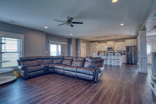 living room with dark wood-type flooring, ceiling fan, plenty of natural light, and decorative columns