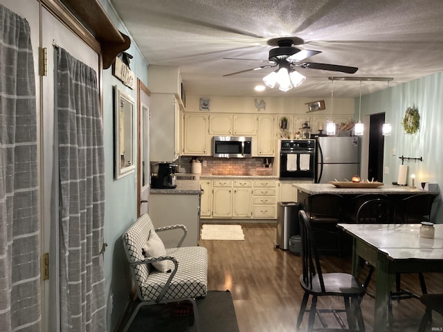 kitchen with hanging light fixtures, appliances with stainless steel finishes, tasteful backsplash, cream cabinetry, and dark hardwood / wood-style flooring