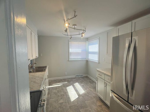 kitchen featuring white cabinets, light stone counters, sink, and stainless steel refrigerator