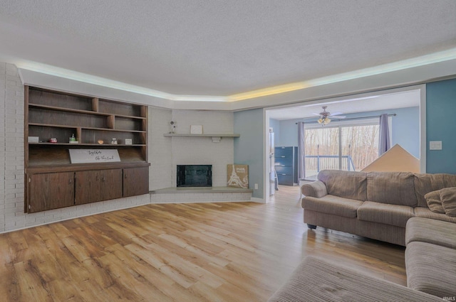 living room featuring ceiling fan, a fireplace, a textured ceiling, and light wood-type flooring