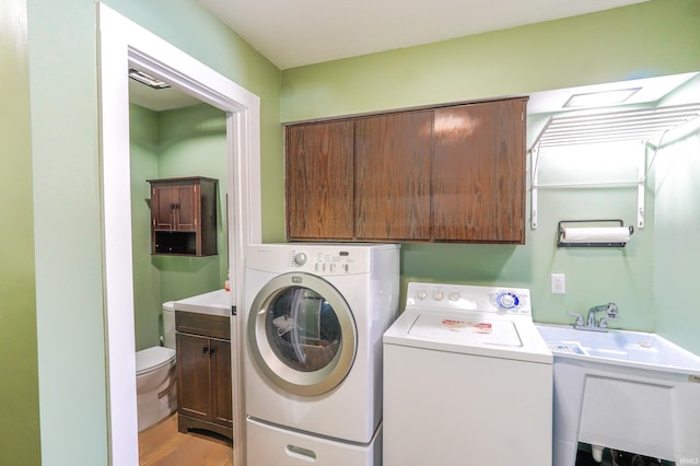 laundry room with cabinets, washing machine and dryer, sink, and light hardwood / wood-style floors