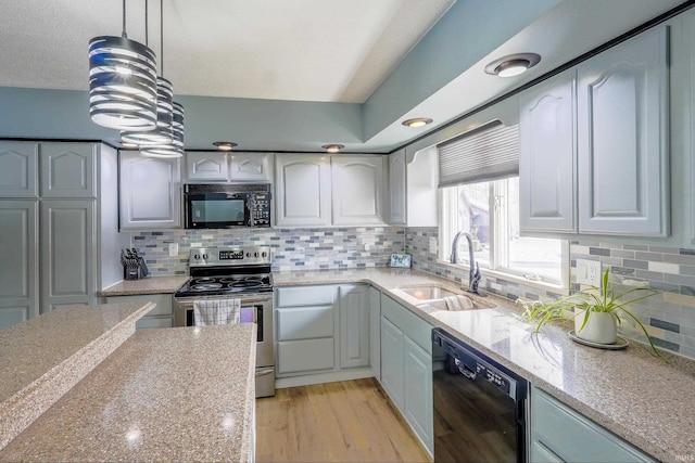 kitchen with sink, light stone counters, hanging light fixtures, light wood-type flooring, and black appliances