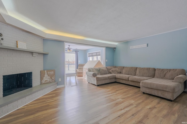 living room with ceiling fan, a brick fireplace, a textured ceiling, and light hardwood / wood-style floors