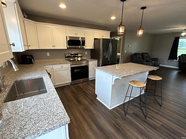 kitchen with stainless steel appliances, sink, white cabinets, a kitchen island, and hanging light fixtures