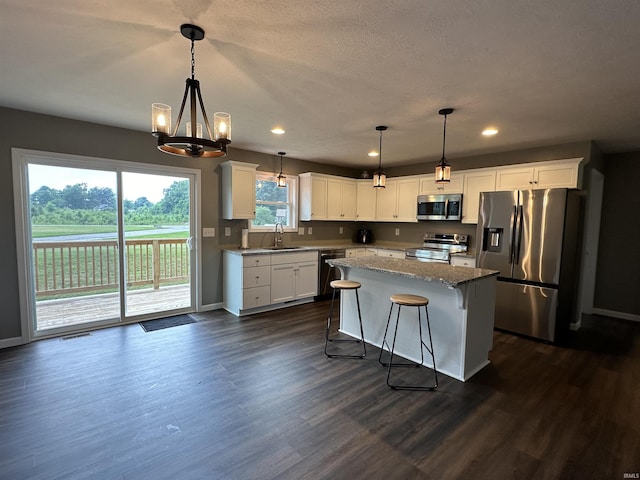 kitchen with appliances with stainless steel finishes, a kitchen island, sink, pendant lighting, and white cabinetry