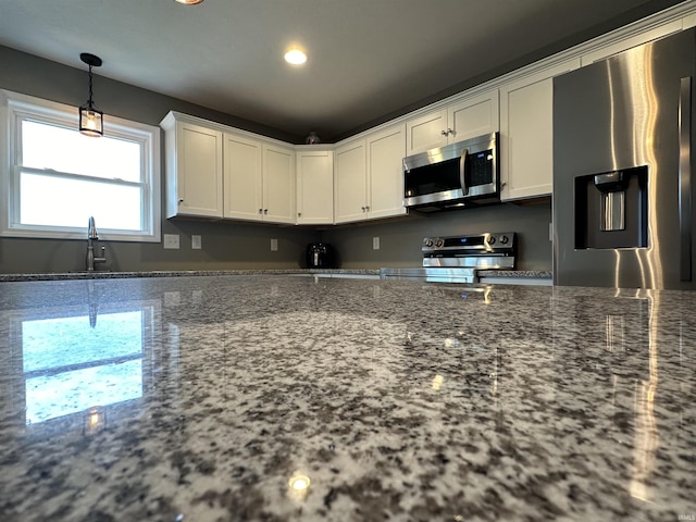 kitchen with appliances with stainless steel finishes, sink, stone countertops, decorative light fixtures, and white cabinets