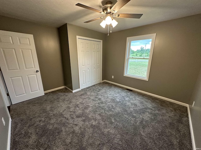 unfurnished bedroom with ceiling fan, a closet, and dark carpet