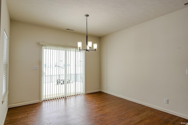 spare room featuring a textured ceiling, an inviting chandelier, and dark wood-type flooring