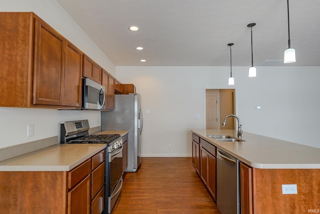 kitchen featuring pendant lighting, dark wood-type flooring, a center island with sink, sink, and stainless steel appliances