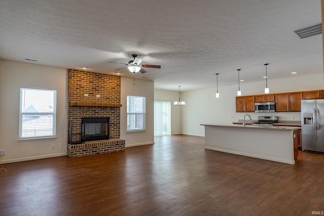 kitchen featuring appliances with stainless steel finishes, dark hardwood / wood-style flooring, ceiling fan with notable chandelier, a center island with sink, and decorative light fixtures