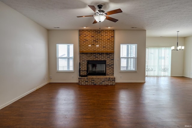 unfurnished living room with a textured ceiling, ceiling fan with notable chandelier, dark wood-type flooring, and a brick fireplace