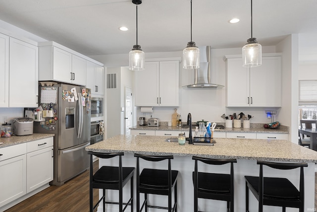 kitchen with a kitchen island with sink, dark wood-type flooring, white cabinets, wall chimney range hood, and stainless steel appliances