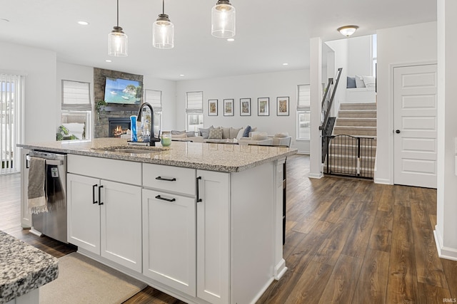 kitchen featuring dishwasher, white cabinets, a center island with sink, sink, and hanging light fixtures