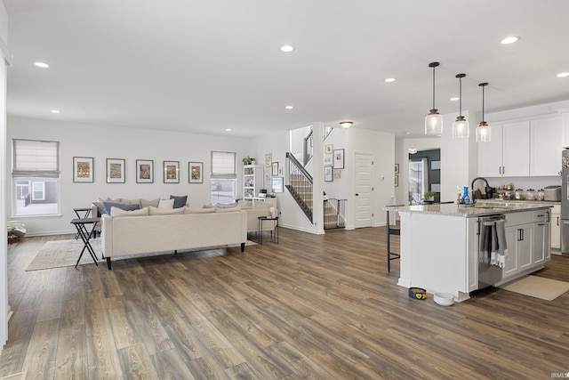 kitchen with dark wood finished floors, open floor plan, stainless steel dishwasher, white cabinetry, and a sink