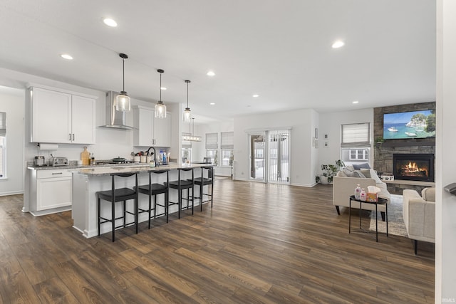 kitchen with a center island with sink, white cabinets, pendant lighting, and wall chimney range hood