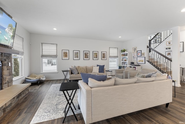 living room with a stone fireplace and dark wood-type flooring